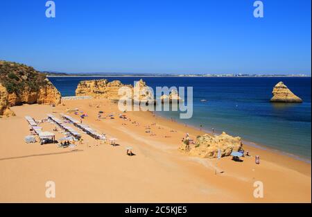 Lagos, Algarve, Portugal. Blick auf die Klippe von oben auf Touristen, die in der warmen Sonne am Dona Ana Strand in Lagos, in der westlichen Algarve, sonnenbaden. Stockfoto