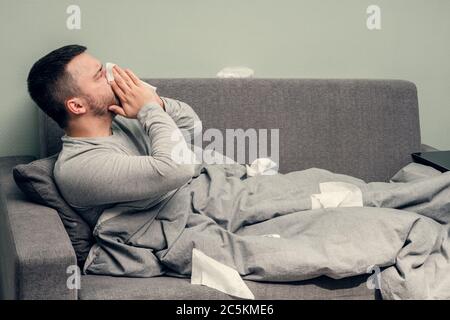 Krankheit. Zu Hause erfreuen. Ein junger Mann ist krank, ist zu Hause behandelt. Bläst ihre Nase in eine Serviette, laufende Nase. Infektion, Epidemie, Bacillus Träger. Stockfoto