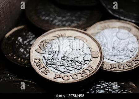 Britische 1-Pfund-Münzen, die in der Box übereinander gelegt werden. Makrofoto mit dramatischen Schatten. Stockfoto