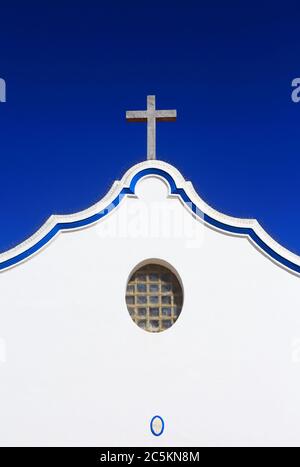 Portugal, Sines, Vila Nova de Milfontes. Unsere Dame der Gnade Kirche. Detail der weiß getünchten Fassade und Granit Kreuz gegen einen klaren blauen Himmel. Stockfoto