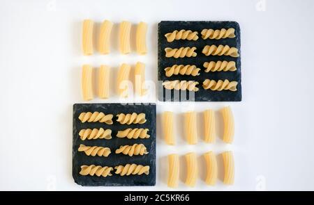 Verschiedene Arten von rohen Pasta auf quadratischen schwarzen Granit Untersetzer und weißem Hintergrund, Food-Knolling-Konzept. Stockfoto