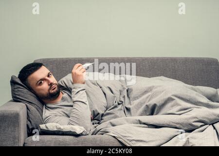 Krankheit. Heitern Sie zu Hause. Ein junger Mann ist krank, wird zu Hause behandelt. Bläst ihre Nase in eine Serviette, laufende Nase. Körpertemperaturmessung. Infektion Stockfoto
