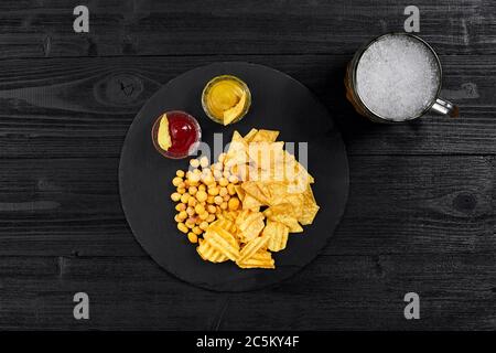 Blick von oben auf Bierglas und Snacks mit Sauce auf schwarzem Holztisch. Stockfoto