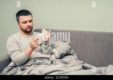 Krankheit. Zu Hause erfreuen. Ein junger Mann ist krank, ist zu Hause behandelt. Bläst ihre Nase in eine Serviette, laufende Nase. Infektion, Epidemie, Bacillus Träger. Stockfoto