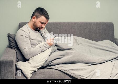 Krankheit. Heitern Sie zu Hause. Ein junger Mann ist krank, wird zu Hause behandelt. Bläst ihre Nase in eine Serviette, laufende Nase. Körpertemperaturmessung. Infektion Stockfoto