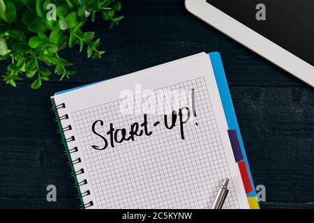 Draufsicht auf offenes Notebook mit Inschrift FÜR DEN START. Grüne Blume, Tablett, Stift und Notizbuch auf Holzgrund. Stockfoto