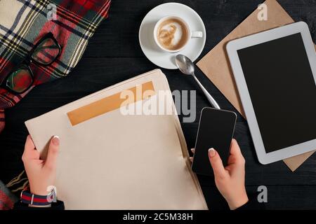 Zeitung und Kaffeetasse, Lesebrille, Notebook, Hände halten Smartphone. Stockfoto