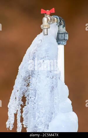 Gefrorener Wasserhahn im Winter. Brauner Hintergrund Stockfoto