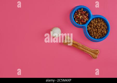 Trockenes Tierfutter in Schale mit einem Ball und Hundeknochen auf rosa Hintergrund Draufsicht Stockfoto