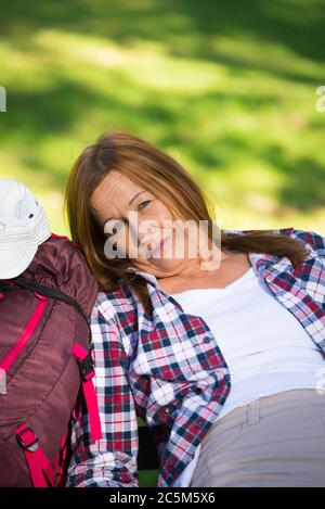 Portrait aktiv Attraktive ältere Frau, die sich auf der Bank ausruhen, erschöpft und müde nach dem Wandern, mit Rucksack im Freien zu Fuß. Stockfoto