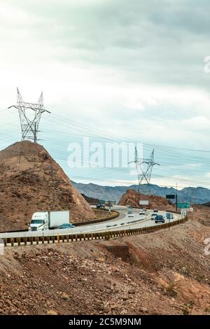 Weißer LKW, der auf einem Wüstenautobahn nahe Mojave, Las Vegas, Nevada, USA vor großen Kabeltürmen fährt. Stockfoto