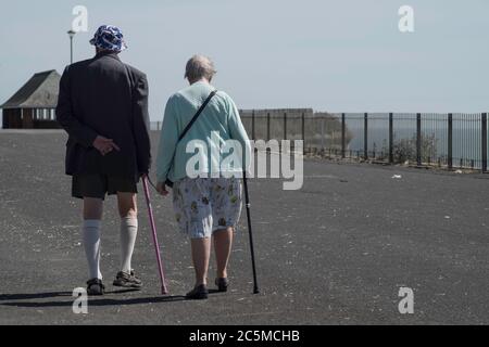 Ältere typisch britische Paare gehen mit Spazierstöcken und Shorts über den Boulevard in der Nähe von Broadstairs Stockfoto