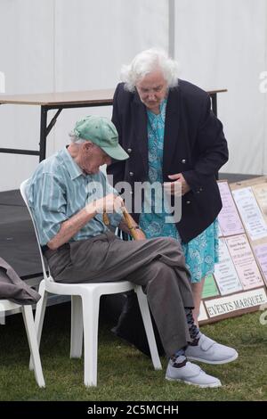 Ältere Paare, die sich auf einer Messe in london unterhalten. Sie steht und er sitzt auf einem Stuhl Stockfoto