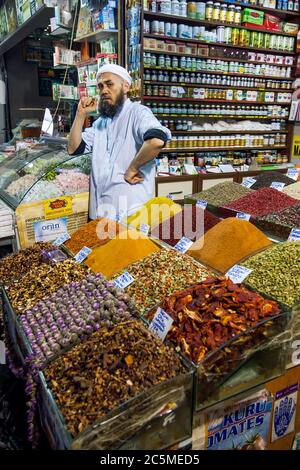 Ein Stallbesitzer, der Trockenfrüchte, Süßigkeiten, Gewürze und Nüsse verkauft, wartet an seiner Ladenfront auf Kunden im Gewürzbasar in Istanbul in der Türkei. Stockfoto