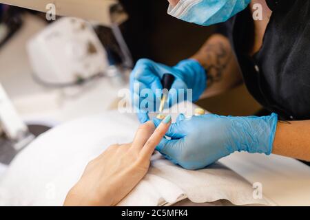 Nahaufnahme der Kosmetikerin, die die Nägel ihrer Kundin mit blauem und gelbem Nagellack malt. Stockfoto