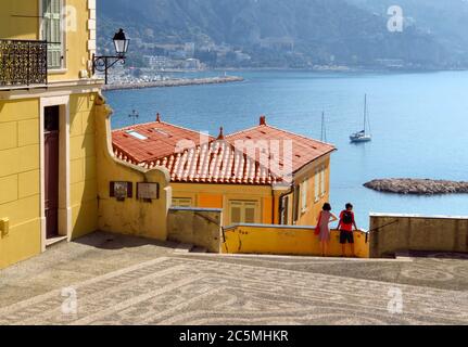 Menton, Frankreich - 30. Juni 2018: Helle Fassaden von bunten Häusern und das blaue Meer an einem sonnigen Tag. Menton ist eine kleine Küstenstadt an der französischen Riviera Stockfoto