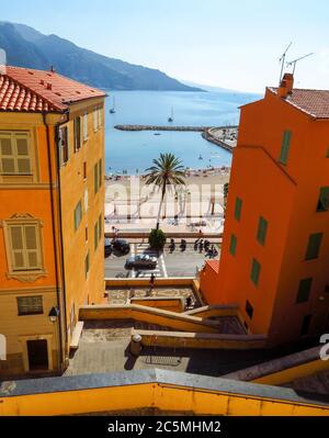 Menton, Frankreich - 30. Juni 2018: Helle Fassaden von bunten Häusern und das blaue Meer an einem sonnigen Tag. Menton ist eine kleine Küstenstadt an der französischen Riviera Stockfoto