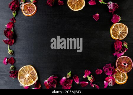 Holzhintergrund mit trockenen Rosen und Blütenblättern und Scheiben von trockenem Orange mit Kopierraum. Flache Lay-Komposition mit Rahmenrand aus trockenen Rosen und Cit Stockfoto