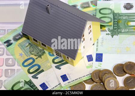 Modellhaus mit (Euro)Banknoten und Münzen als Symbolbild für hohe Immobilienpreise Stockfoto