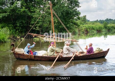 Eine Gruppe von Männern in Kleidung der Wikingerzeit (9-11 Jahrhundert) rudern auf Rudern in einem alten Boot. Die Frau winkt mit der Hand. Stockfoto