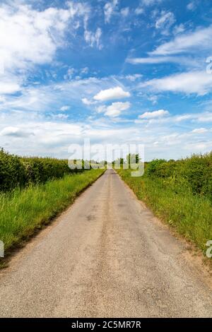 Blick entlang einer schmalen Landstraße an einem sonnigen Sommertag Stockfoto