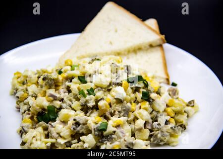 Ukrainischer und russischer Salat Olivier nach einem neuen Rezept auf einem weißen Teller. Gesunder Salat Olivier mit Fleisch, Mais und Scheiben Weißbrot. Delic Stockfoto