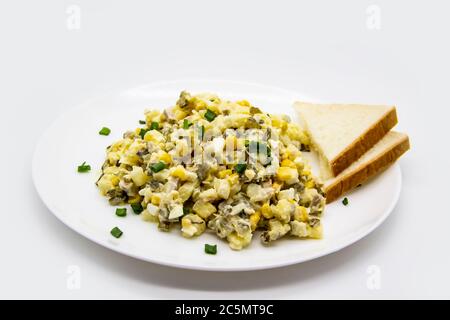 Ukrainischer und russischer Salat Olivier nach einem neuen Rezept auf einem weißen Teller. Gesunder Salat Olivier mit Fleisch, Mais und Scheiben Weißbrot. Delic Stockfoto