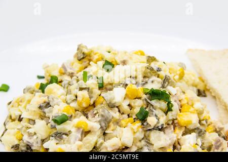 Ukrainischer und russischer Salat Olivier nach einem neuen Rezept auf einem weißen Teller. Gesunder Salat Olivier mit Fleisch, Mais und Scheiben Weißbrot. Delic Stockfoto