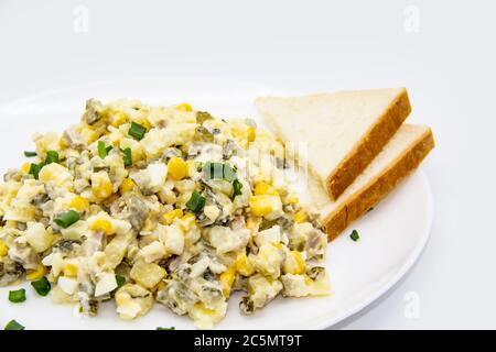 Ukrainischer und russischer Salat Olivier nach einem neuen Rezept auf einem weißen Teller. Gesunder Salat Olivier mit Fleisch, Mais und Scheiben Weißbrot. Delic Stockfoto