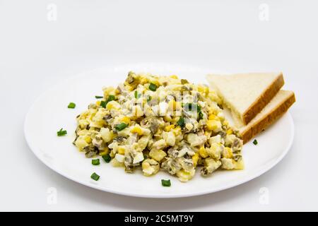Ukrainischer und russischer Salat Olivier nach einem neuen Rezept auf einem weißen Teller. Gesunder Salat Olivier mit Fleisch, Mais und Scheiben Weißbrot. Delic Stockfoto