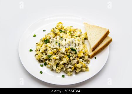 Ukrainischer und russischer Salat Olivier nach einem neuen Rezept auf einem weißen Teller. Gesunder Salat Olivier mit Fleisch, Mais und Scheiben Weißbrot. Delic Stockfoto