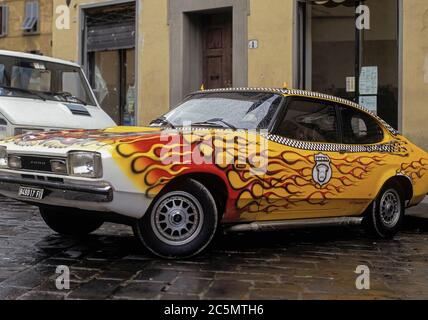 Ein Ford Capri, in flammenden Rot- und Gelbtönen gestaltet und mit Teufelshörnern auf dem Dach ausgestattet, bietet Taxifahrten mit dem „Hell's Cab 666“ an. Geparkt an einem regnerischen Tag im Oktober 1996 auf der Piazza di Santo Spirito, Oltrarno, Florenz, Toskana, Italien. Stockfoto