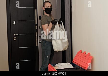 Ein maskiertes Mädchen nimmt Waren und Produkte von einem Kurier in einer Pandemie und Quarantäne. Stockfoto