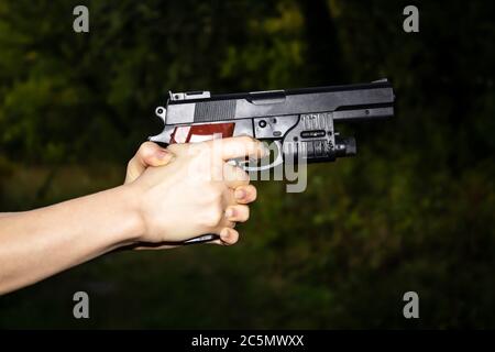 Weibliche Hände halten eine Waffe auf einem dunklen Hintergrund. Eine gefährliche Situation mit einer Waffe Stockfoto
