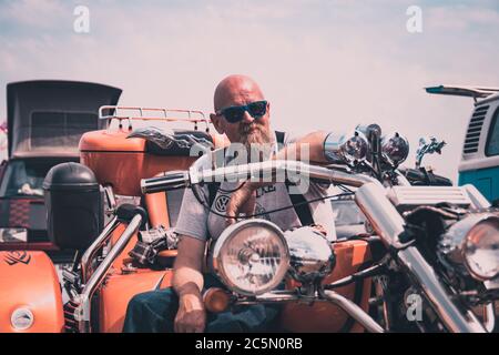 Ein Biker mittleren Alters auf seinem Motorrad mit dem Arm am Lenker Stockfoto