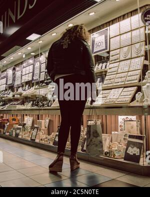 Eine junge Frau mit einer Einkaufstasche suchen im Fenster eines Schmuck Shop im guten auf Verkauf Stockfoto