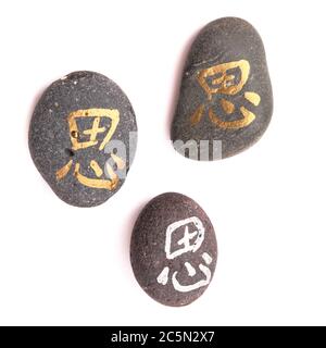 Chinesisches Zeichen xi oder japanisches Iki, was Ruhe bedeutet, geschrieben auf einem Kieselstein, isoliert auf weiß Stockfoto