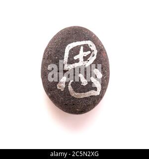 Chinesisches Zeichen xi oder japanisches Iki, was Ruhe bedeutet, geschrieben auf einem Kieselstein, isoliert auf weiß Stockfoto