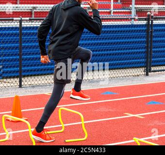 Ein High School-Läufer überwindet beim Speed- und Agility-Workout gelbe Mini-Hürden. Stockfoto