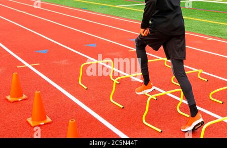 Rückansicht eines High School Track and Field Athlet läuft über gelbe Hürden in Lane auf einer roten Strecke aufgestellt. Stockfoto