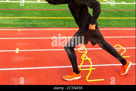 Ein High School Junge läuft über Mini-Hurldes auf einer roten Spur während Track and Field Practice. Stockfoto