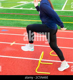 Ein Teenager-Mädchen der High School übertritt während der Trainings-und Feldübungen die gelben Mini-Bananenhals-Hürden in der A-Position. Stockfoto