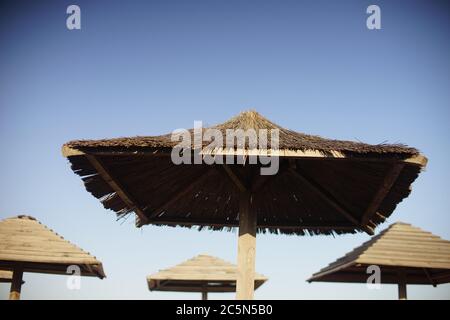 Strohdächer am Strand gegen den blauen Himmel. Stockfoto