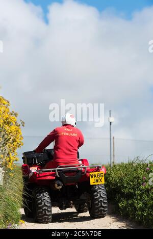 Ein RNLI Rettungsschwimmer auf einem Quad-Bike entlang des Küstenweges bei Fistral in Newquay in Cornwall. Stockfoto