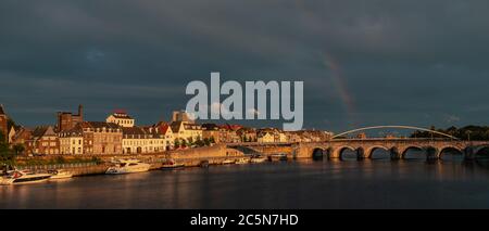 Skyline von Maastricht mit dem kommenden Gebiet Wyck und der Sint Servaas Brücke nach einem Sommerabend Sturm in der goldenen Stunde mit einem Regenbogen zeigen Stockfoto