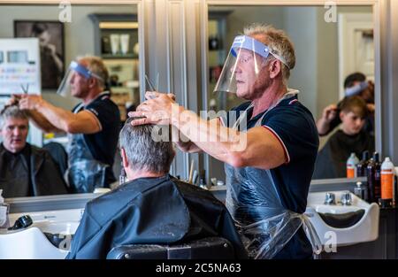Harrogate, North Yorkshire, Großbritannien. Juli 2020. David Steca, Eigentümer des Barbiers Steca N.6, ist bei der Arbeit und trägt vollständige PSA, während die Barbiere am Super-Samstag wieder für die Öffentlichkeit zugänglich sind. Kredit: ernesto rogata/Alamy Live Nachrichten Stockfoto