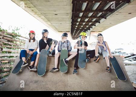 Gruppe von Freunden Kinder an Skate Rampe. Porträt von selbstbewussten frühen Teenager-Freunden, die im Freiluftstadtskate-Park herumhängen. Kleine Skateboarder Stockfoto