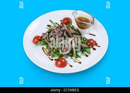 Rucola-Salat mit Rindzunge und Honig-Senf-Sauce auf blau isoliert Stockfoto