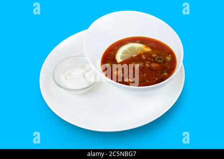 Solyanka, würzige und saure russische rote Suppe mit Zitrone isoliert auf blauem Hintergrund Stockfoto