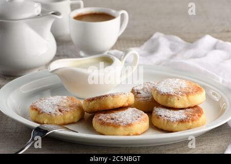 Frühstück. Käse Pfannkuchen mit saurer Sahne mit Puderzucker auf einem weißen Teller bestreut. Stockfoto